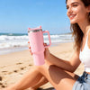 A-SUB pink insulated tumbler for UV printing held by a woman sitting on the beach, showcasing its stylish design.